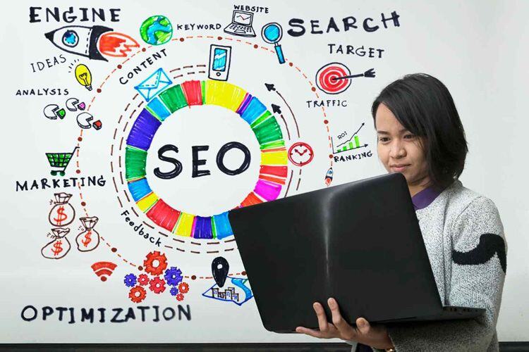 Mujer sostiene portatil en sus manos…al fondo se lenn textos como: SEO, Engine, Target, marketing y content