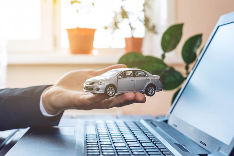 Mano de hombre sostiene un carro en miniatura sobre el teclado de un computador